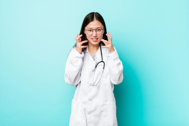 Joven médico chino mujer molesta gritando con las manos tensas.