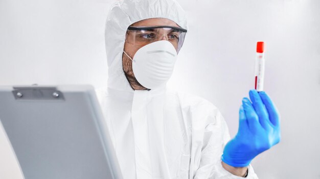 Joven médico científico en traje de protección química con tubo de ensayo en el laboratorio