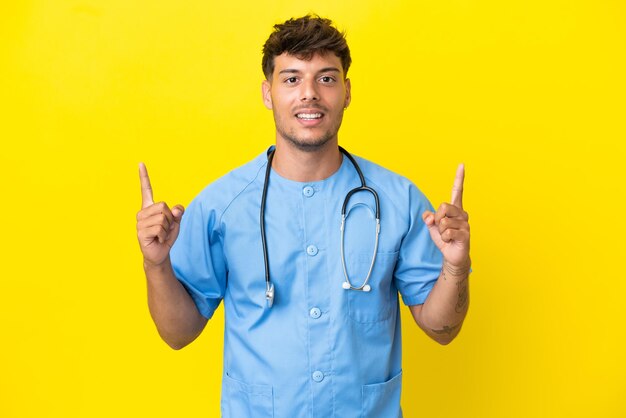 Joven médico cirujano hombre aislado de fondo amarillo señalando una gran idea