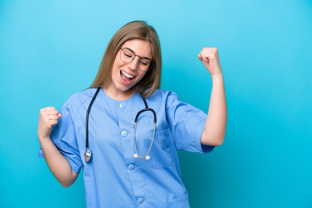 Joven médico cirujano mujer aislada de fondo azul celebrando una victoria