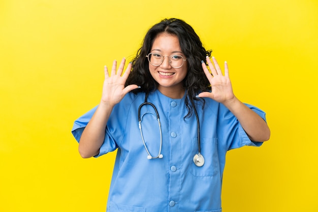 Joven médico cirujano mujer asiática aislada sobre fondo amarillo contando diez con los dedos