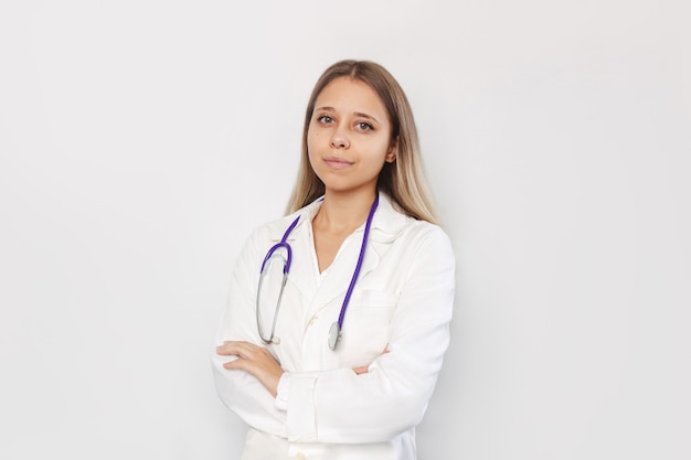 Un joven médico emale en una bata blanca con estetoscopio alrededor de su cuello se encuentra con las manos cruzadas