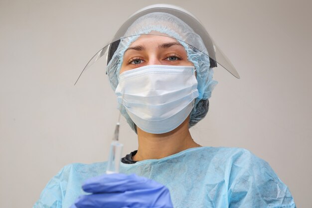 Joven médico enfermera en una máscara protectora con una jeringa en la mano