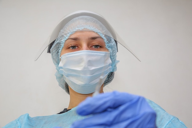 Joven médico enfermera en una máscara protectora con una jeringa en la mano