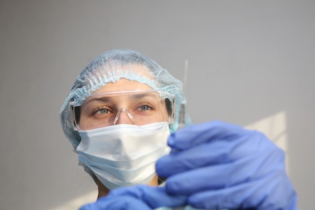 Joven médico enfermera en una máscara protectora con una jeringa en la mano