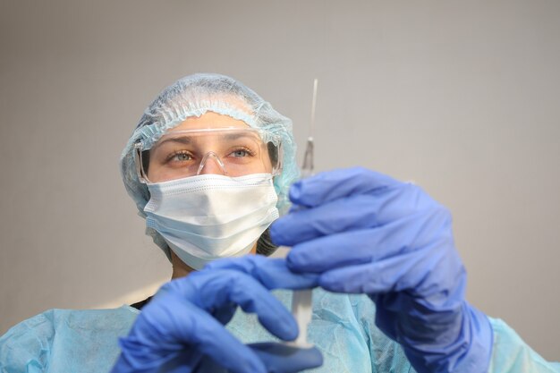 Joven médico enfermera en una máscara protectora con una jeringa en la mano