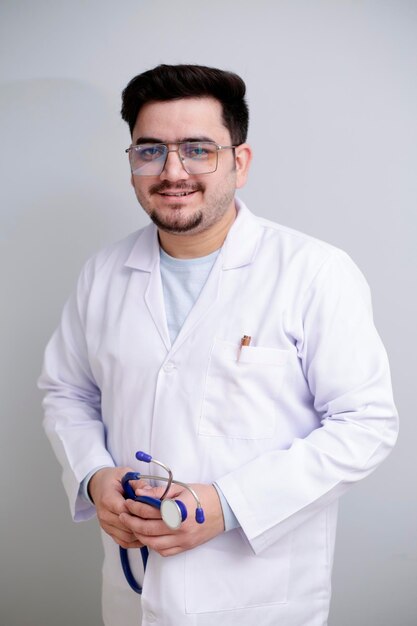 Un joven médico está de pie y sosteniendo un estetoscopio en la mano y sonriendo