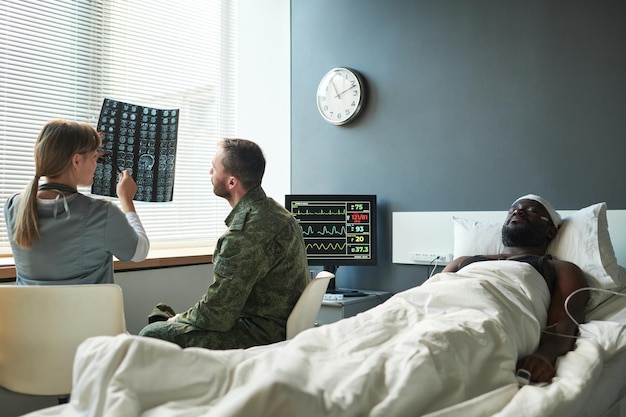 Joven médico explicando los detalles del escáner cerebral a un soldado con uniforme militar