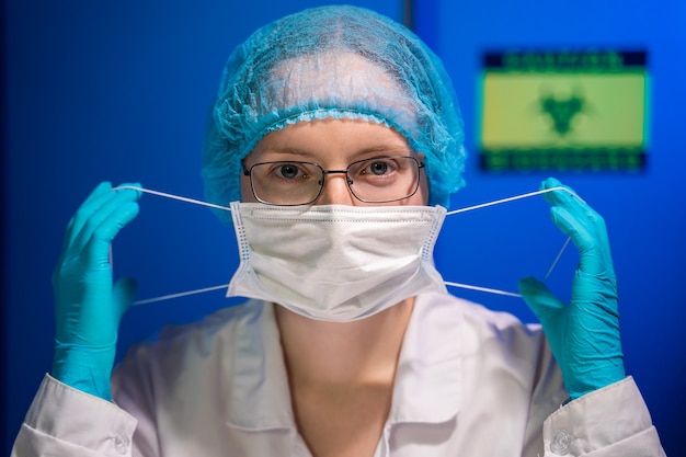 Un joven médico con gafas, guantes y un gorro médico se pone una máscara protectora