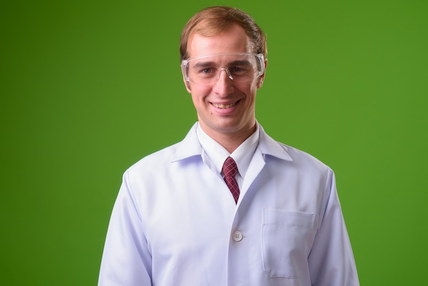 Joven médico con gafas protectoras contra la pared verde