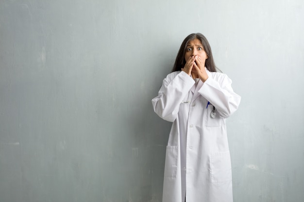 Joven médico india contra una pared muy asustada y asustada, desesperada por algo, gritos de sufrimiento y ojos abiertos, concepto de locura.