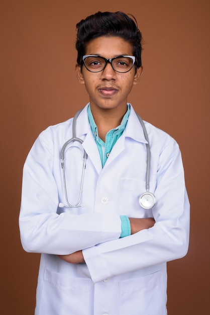 Joven médico indio con anteojos contra el fondo marrón