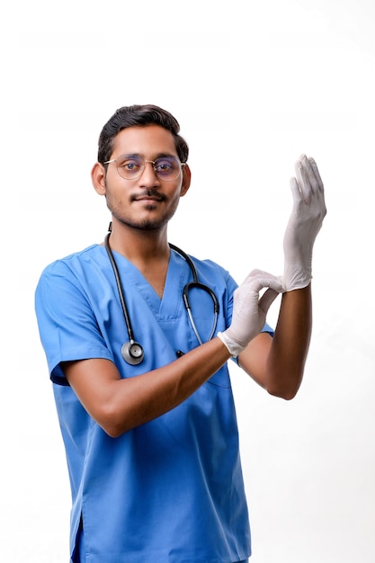 Joven médico indio poniéndose guantes protectores aislados sobre fondo blanco.