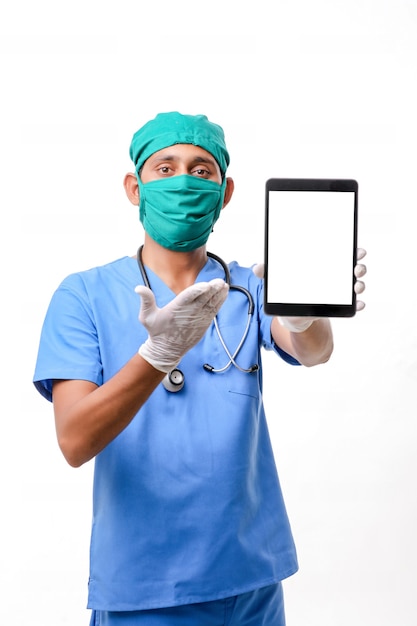 Joven médico indio que muestra la pantalla de la tableta sobre fondo blanco.