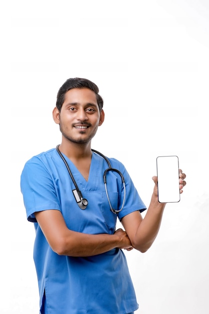 Joven médico indio que muestra la pantalla del teléfono inteligente sobre fondo blanco.