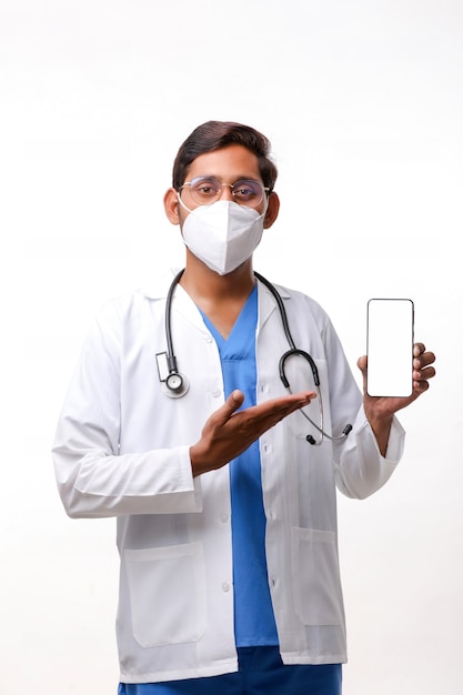 Foto joven médico indio que muestra la pantalla del teléfono inteligente sobre fondo blanco.