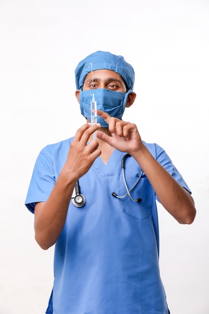 Joven médico indio sosteniendo la jeringa cargada en la mano sobre fondo blanco.