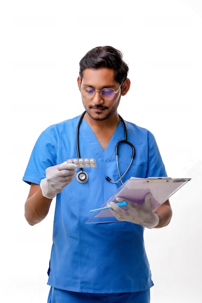 Joven médico indio vestido de uniforme con estetoscopio tomando notas en el Bloc de notas aislado sobre fondo blanco.