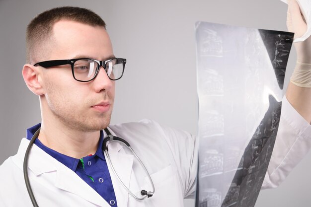 Joven médico masculino mirando una radiografía en un hospital en un retrato de fondo blanco de un especialista