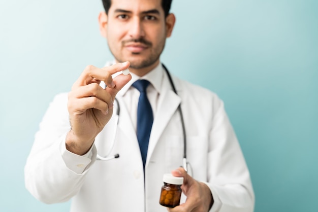 Joven médico masculino que muestra la píldora mientras receta medicamentos en el estudio