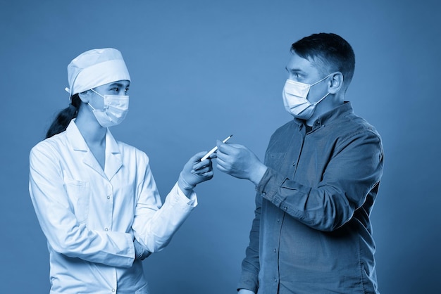 Joven médico midiendo la temperatura de un paciente con un termómetro en un estudio en un fondo azul