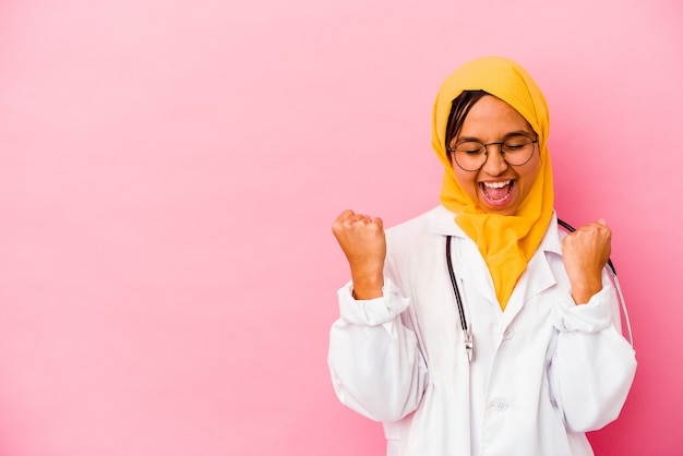 Joven médico mujer musulmana aislada en la pared rosa levantando el puño después de una victoria, concepto ganador