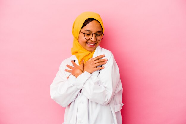 Joven médico mujer musulmana aislada sobre fondo rosa abrazos, sonriendo despreocupada y feliz.