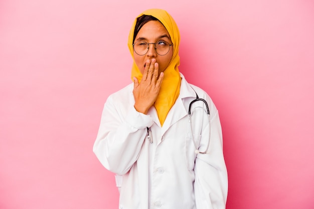 Joven médico mujer musulmana en bostezo rosa mostrando un gesto cansado cubriendo la boca con la mano.