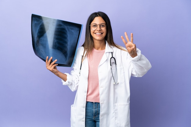 Joven médico mujer sosteniendo una radiografía feliz y contando tres con los dedos