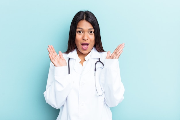 Joven médico mujer venezolana aislada sobre fondo azul sorprendido y consternado.