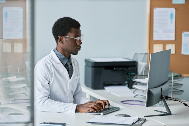 Joven médico negro usando computadora en el escritorio en la oficina trabajando en la clínica