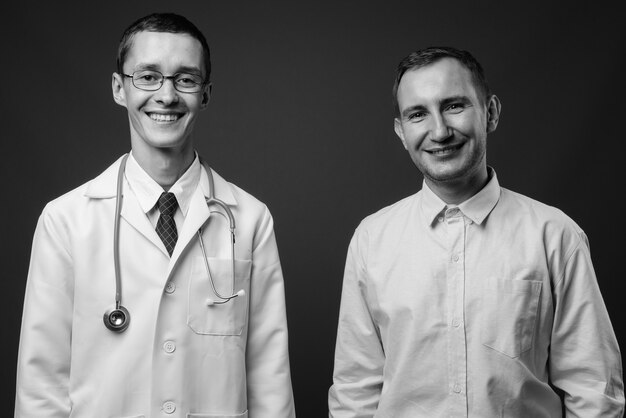 Joven médico y paciente hombre contra la pared gris en blanco y negro