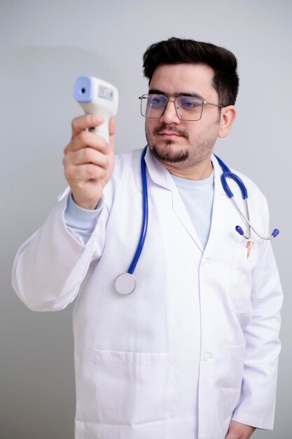 Foto un joven médico está de pie y sosteniendo un termómetro digital en la mano.