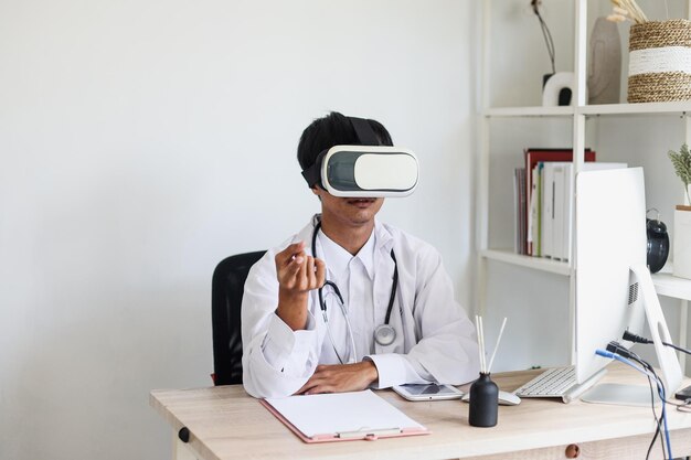 El joven médico que usa gafas VR está sentado y gesticulando con las manos explicando el aprendizaje médico en línea.