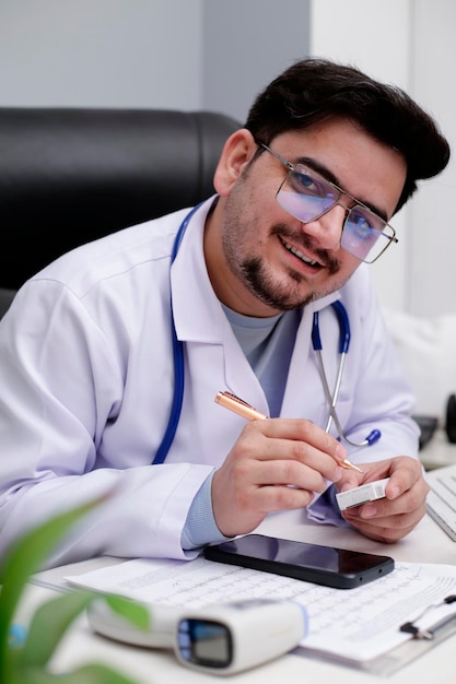 Foto un joven médico está sentado en la clínica con un bolígrafo y un medicamento en la mano.