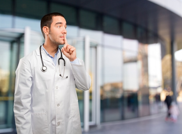 Joven médico serio haciendo un gesto de silencio