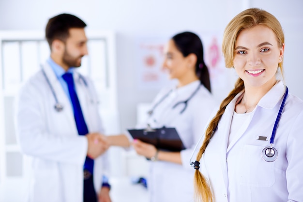 Joven médico sonriendo en el hospital y personal médico revisando registros médicos