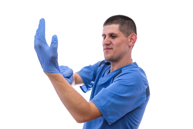 Joven médico en uniforme preparándose para trabajar poniéndose guantes aislado sobre un fondo blanco.