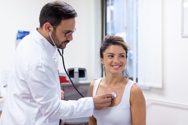 Foto joven médico está usando un estetoscopio para escuchar los latidos del corazón del paciente toma de un médico que le da un chequeo a una paciente