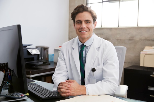 Joven médico varón blanco en el retrato de escritorio