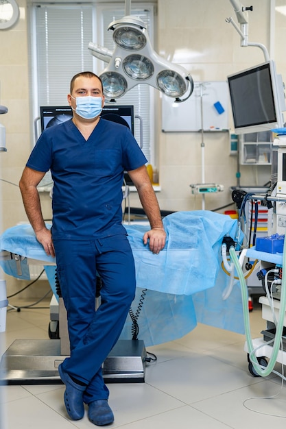 Joven médico varón confiado posa para la cámara en el fondo de la sala de cirugía moderna. Concepto de salud y salvamento.