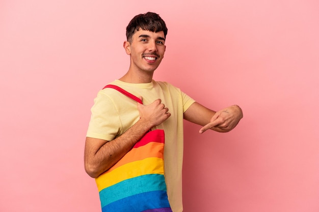 Joven mestizo hombre vestido con bolsa LGTB aislado sobre fondo de color rosa