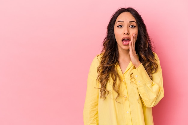 Joven mexicana aislada en la pared rosa grita fuerte, mantiene los ojos abiertos y las manos tensas.