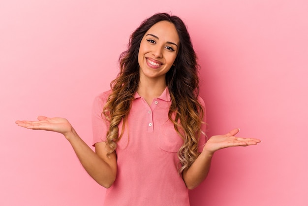 Joven mexicana aislada en pared rosa hace escala con los brazos, se siente feliz y confiada.