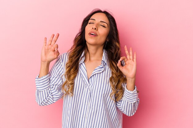 Joven mexicana aislada en la pared rosa se relaja después de un duro día de trabajo, ella está realizando yoga.