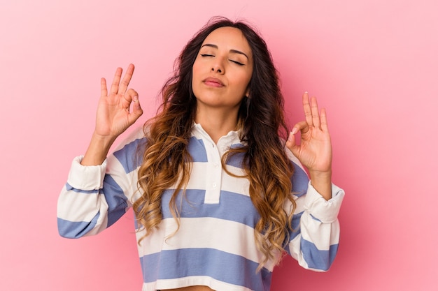 Joven mexicana aislada sobre fondo rosa se relaja después de un duro día de trabajo, ella está realizando yoga.