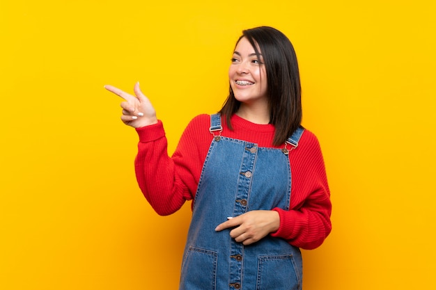 Joven mexicana con un mono sobre una pared amarilla apuntando con el dedo hacia un lado