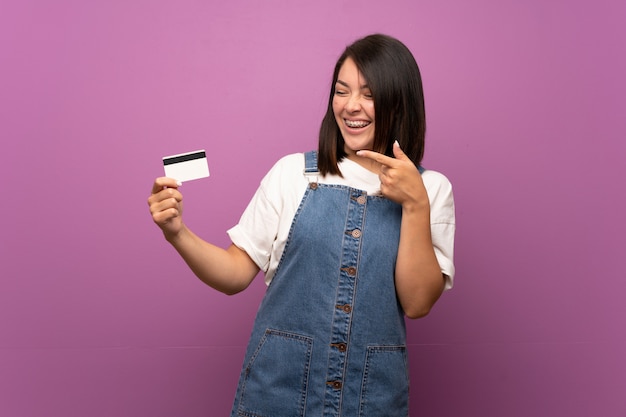 Joven mexicana sobre aislado sosteniendo una tarjeta de crédito