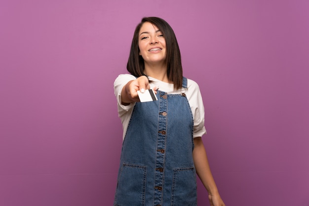 Joven mexicana sobre pared aislada con una tarjeta de crédito