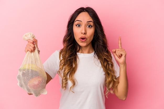 Joven mexicana sosteniendo una bolsa de fruta aislada sobre fondo rosa con una gran idea, concepto de creatividad.